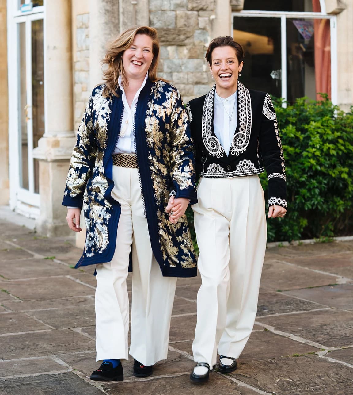 Brides wearing matching wedding outfits: embroidered jackets, white trousers and loafers