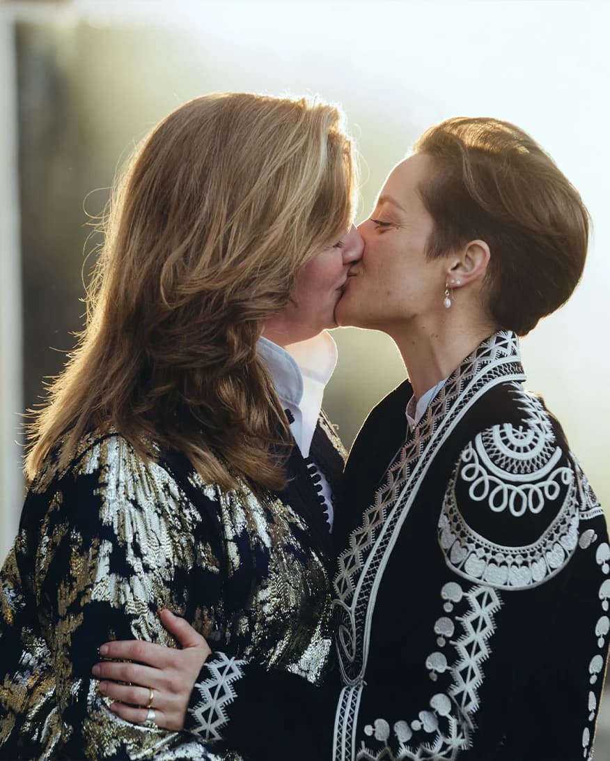 Brides wearing matching embroidered jackets kiss together