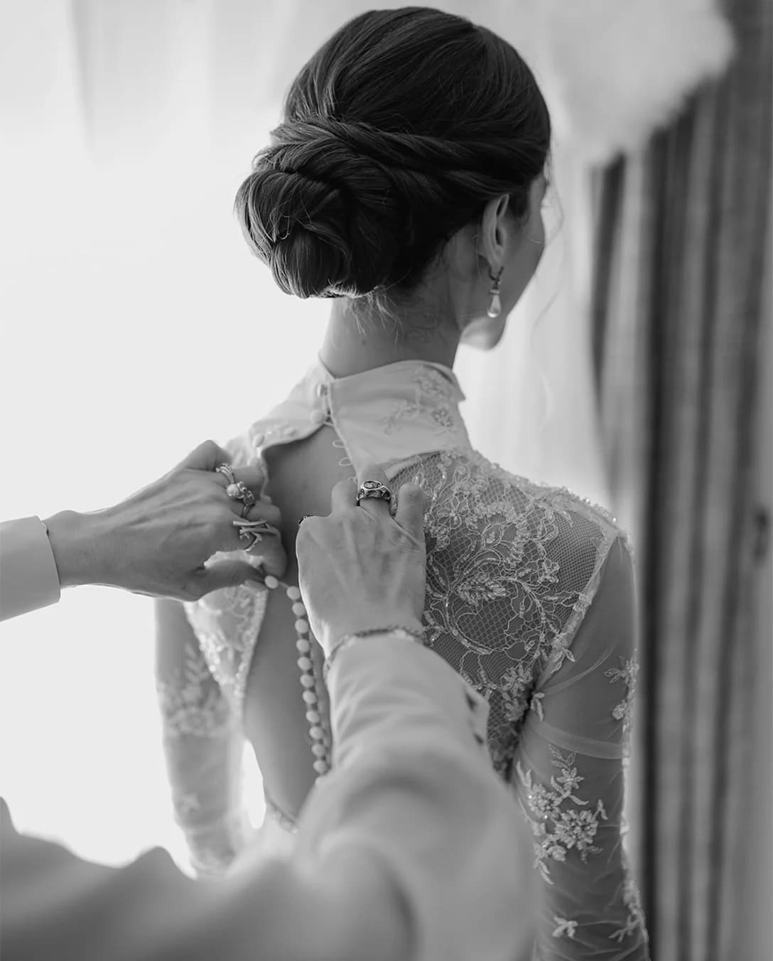 Mother helps bride to put on her embroidered wedding dress