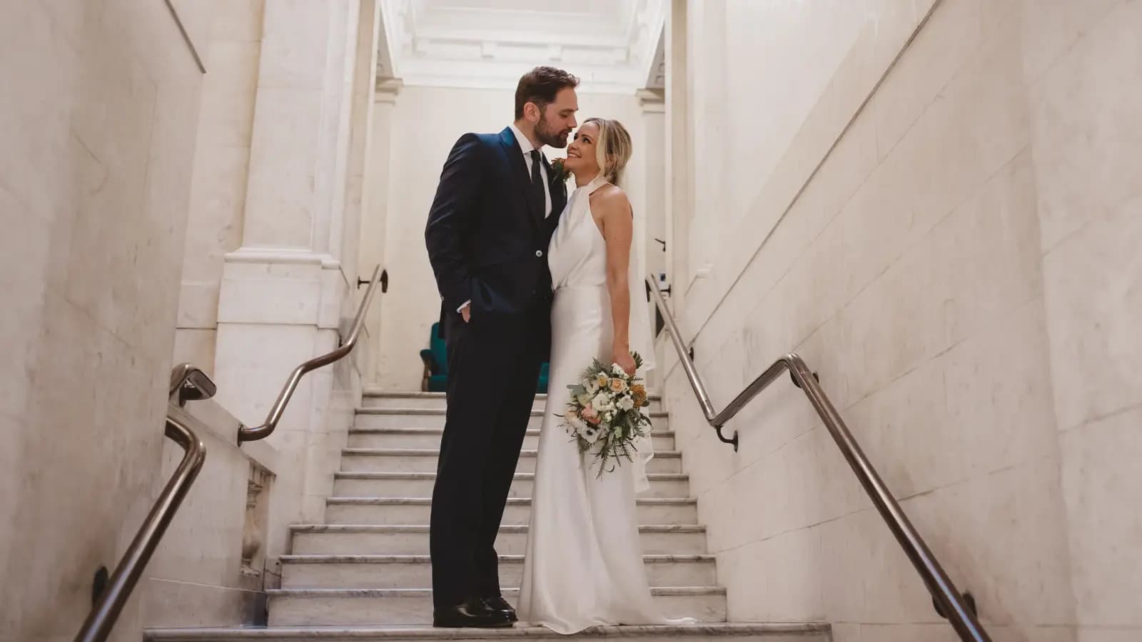 Bride and groom stand on the stairs inside Old Marylebone Town Hall