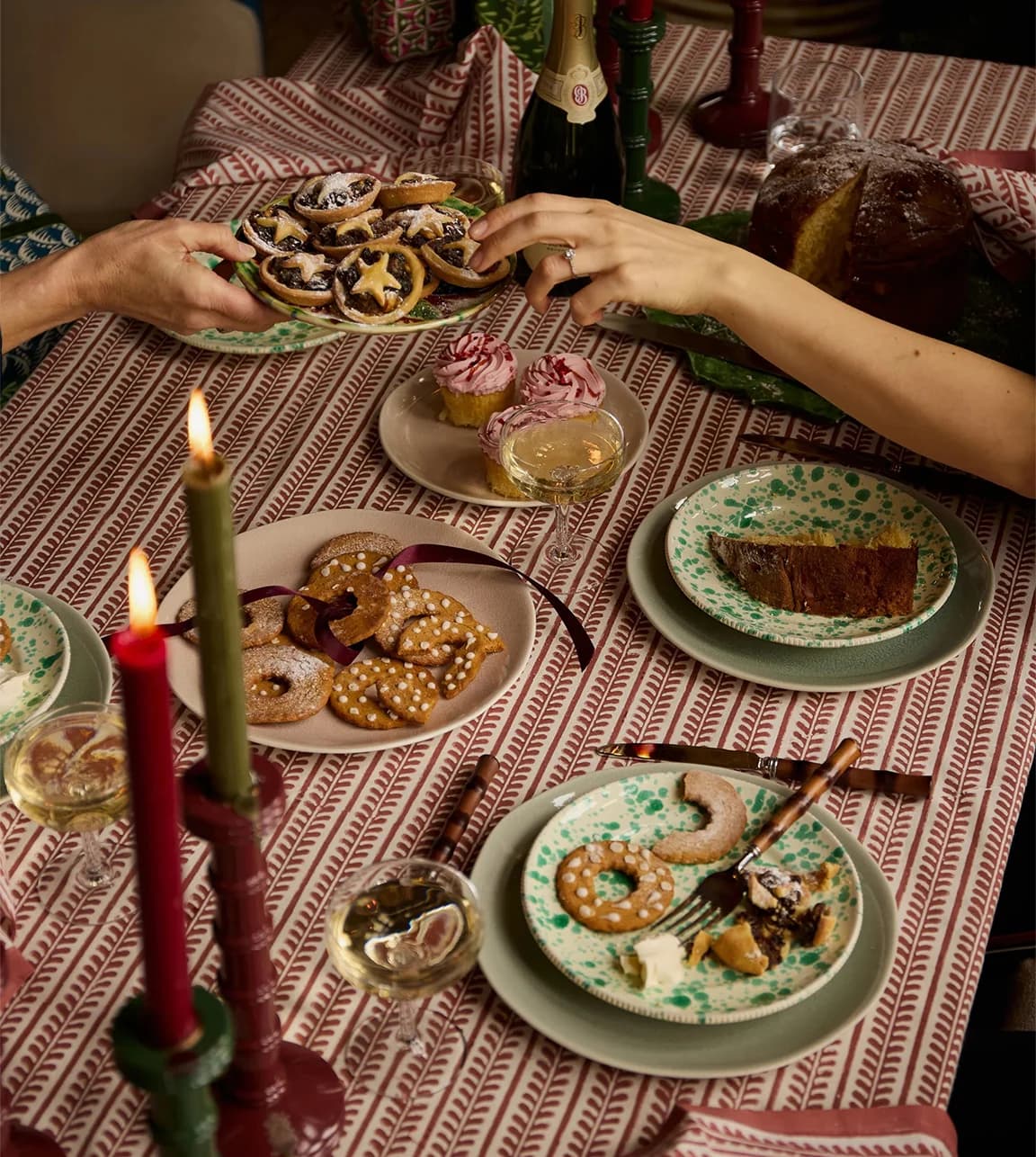 A Christmas table set with mismatched plates and candleholders placed on red hand-printed tablecloth