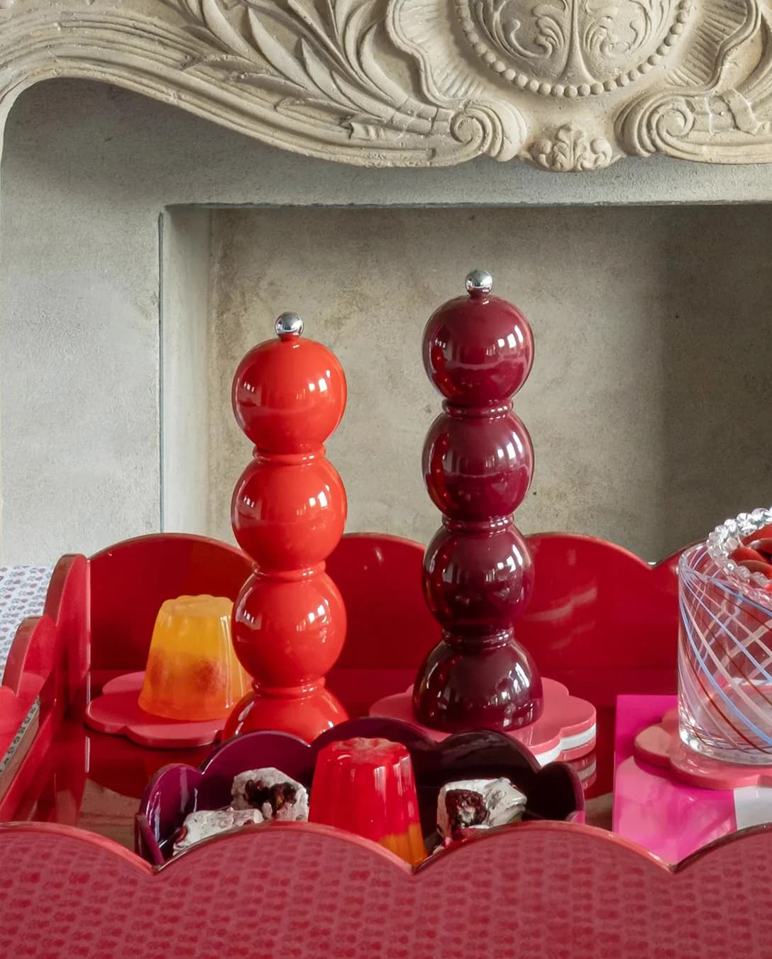 Red lacquered pepper mills placed on scalloped tray 
