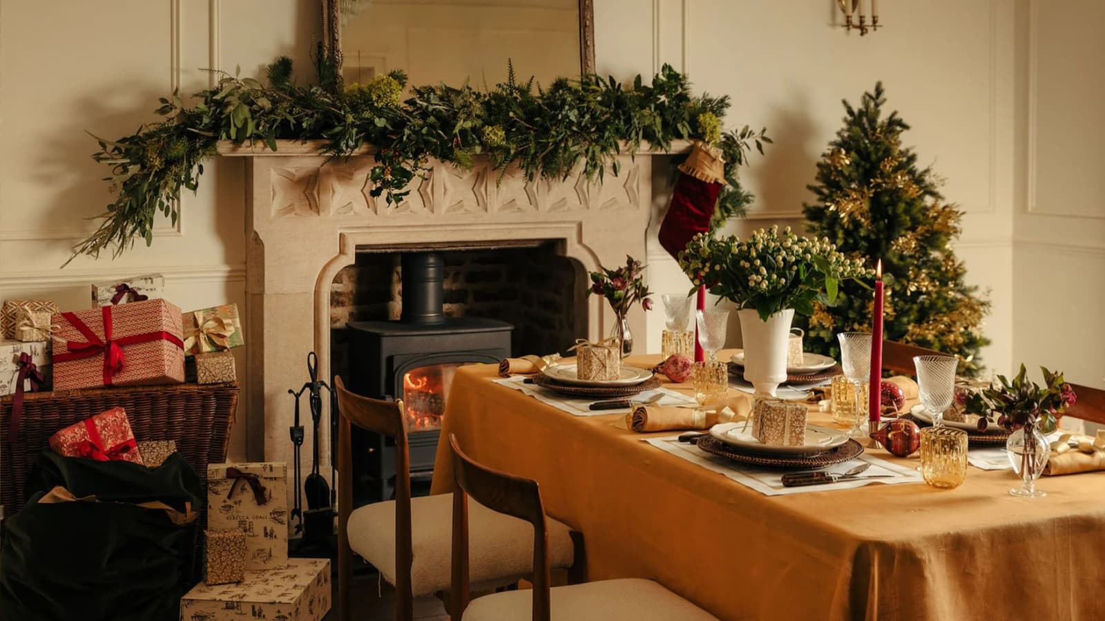 A luxury table setting next to a fireplace decorated with foliage and gift-wrapped presents