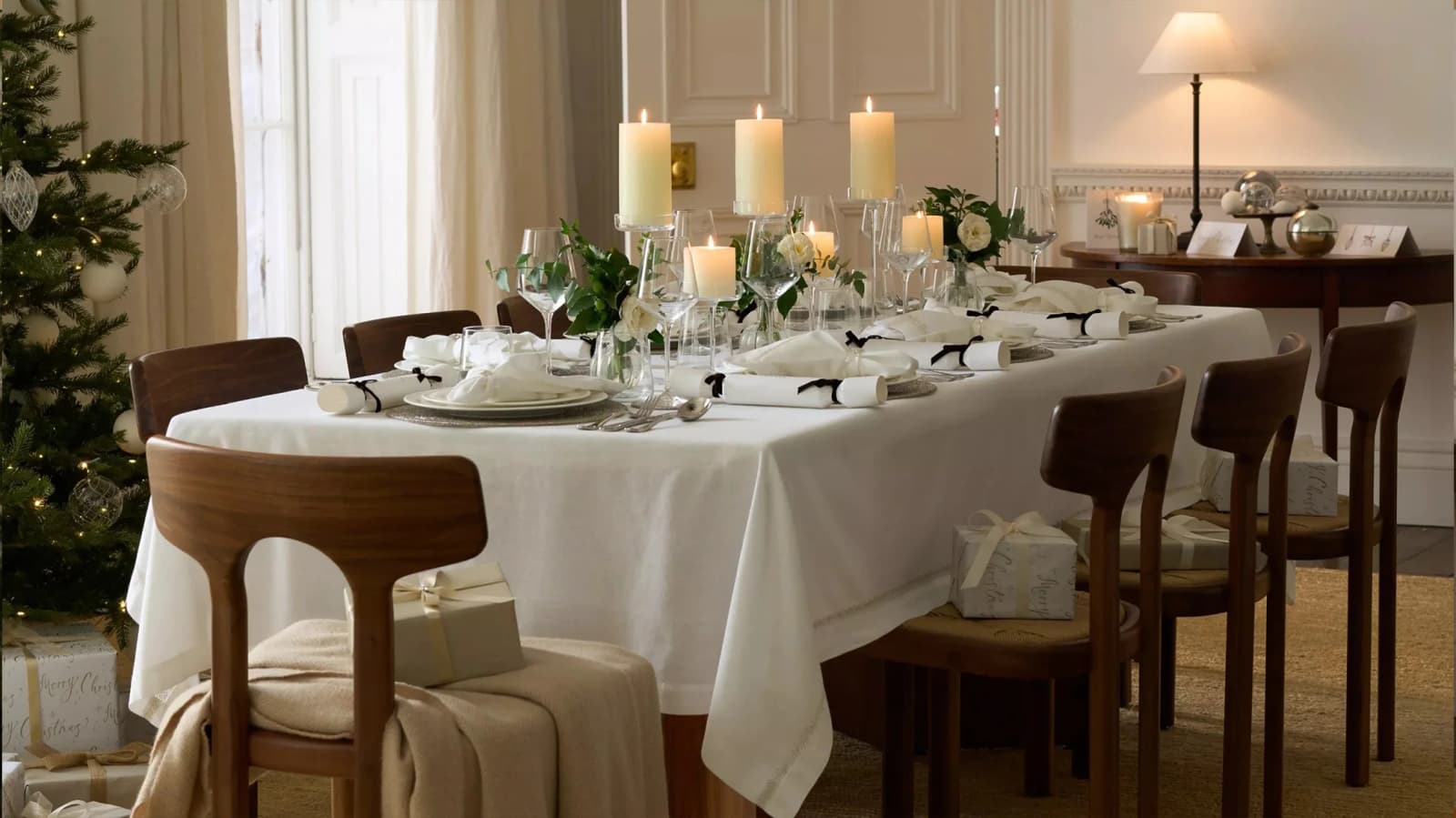 Simple but elegant Christmas table setting with pillar candles, white tablecloth and crackers