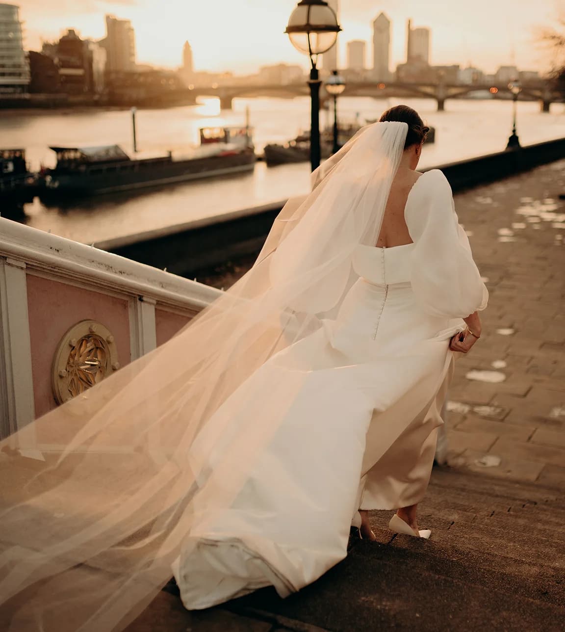 Bride wearing veil and flowy dress walks down the stairs next to Thames