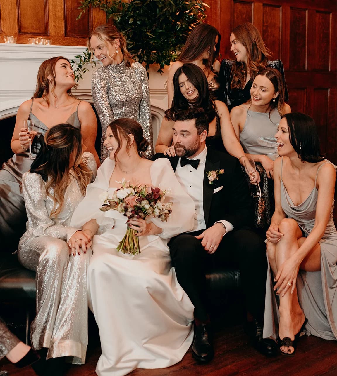 Bride and groom pose with group of bridesmaids that are wearing silver, sparkling and metallic colour dresses
