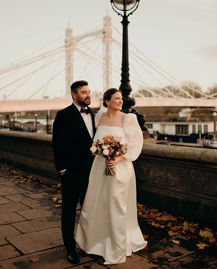 Bride and groom stand next to Thames, in front of the bridge in London
