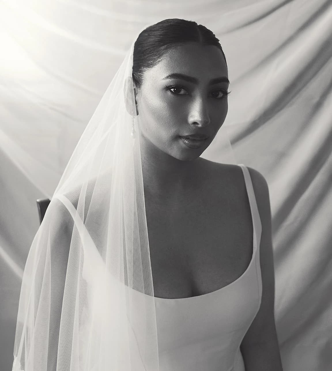 Bride wearing a minimalist gown and sheer veil, posed against softly draped fabric