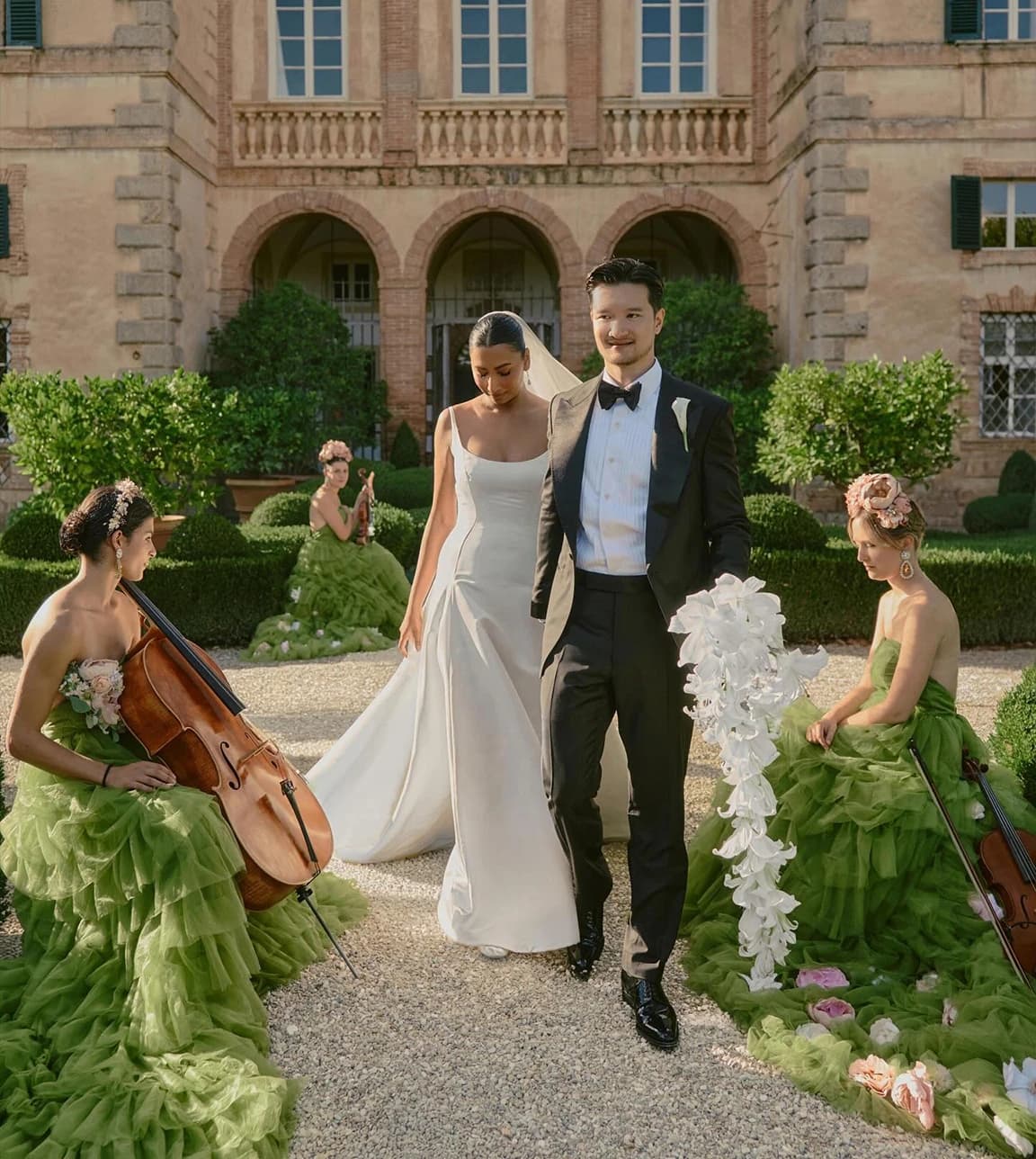 Elegant Italian villa wedding scene with the couple walking through a courtyard, surrounded by musicians in voluminous green gowns and lush garden details.  Select 77 more words to run Humanizer.