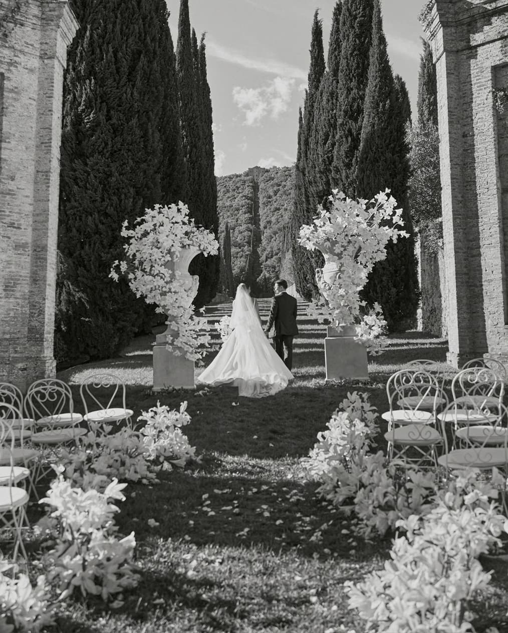 Wedding scene at an Villa Centinale, featuring a cypress-lined aisle adorned with white floral arrangements and the couple walking away together