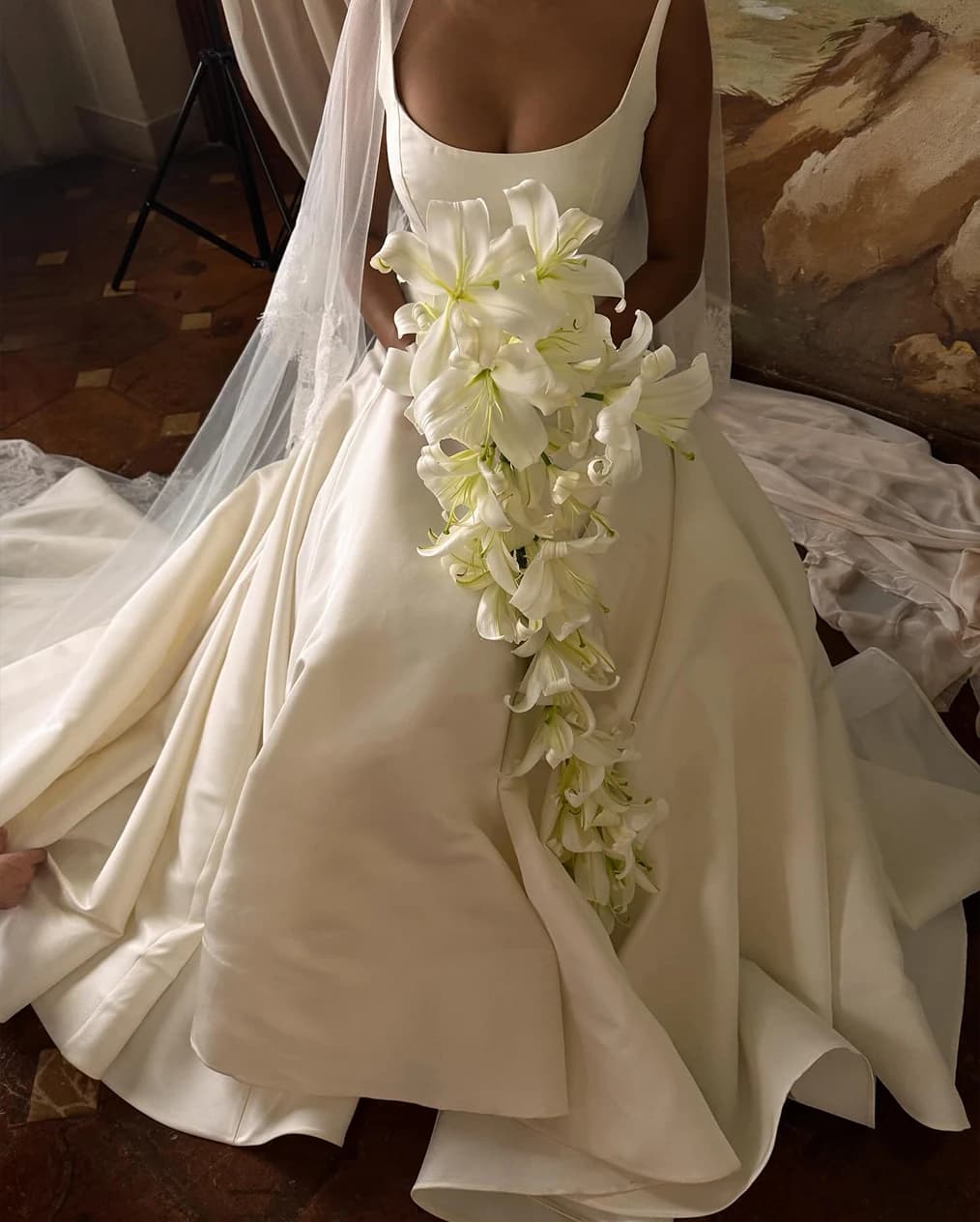 Bride in a minimalist gown holding a cascading bouquet of white lilies, with soft draping and a sheer veil creating an elegant, timeless look.