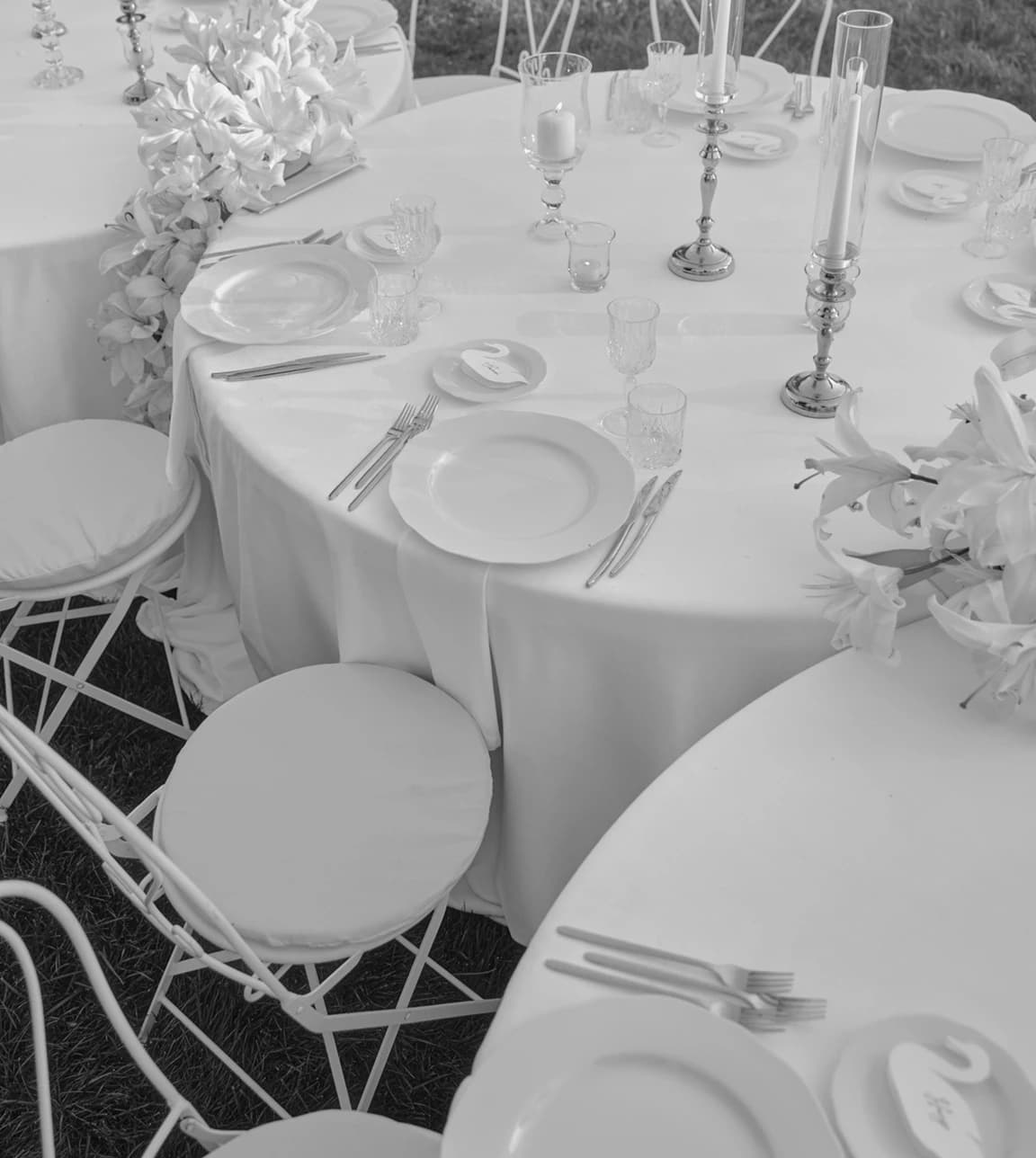 Elegant wedding tablescape with refined place settings, featuring swan-shaped place cards on crisp white linens alongside glassware and soft floral accents.