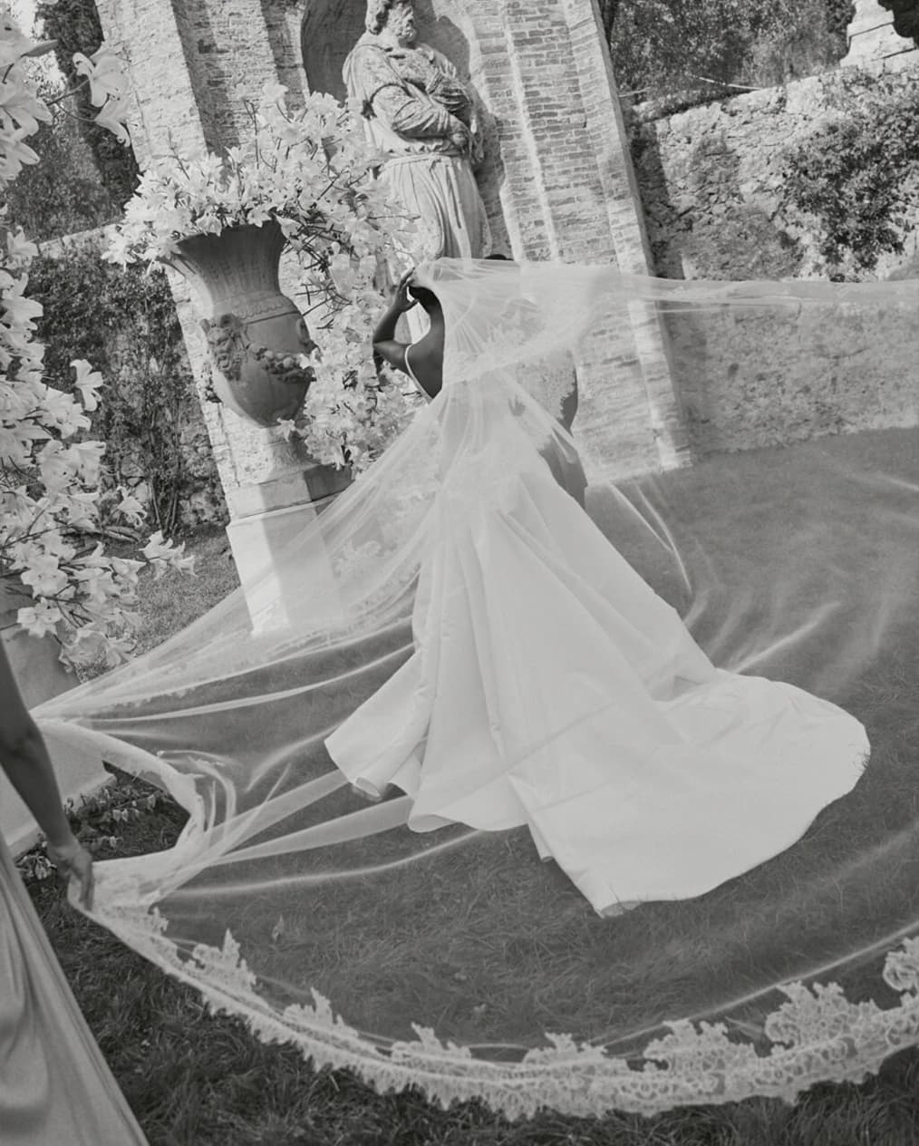 A bridal moment with a flowing veil caught in motion, set against an ornate floral altar and historic stone backdrop.