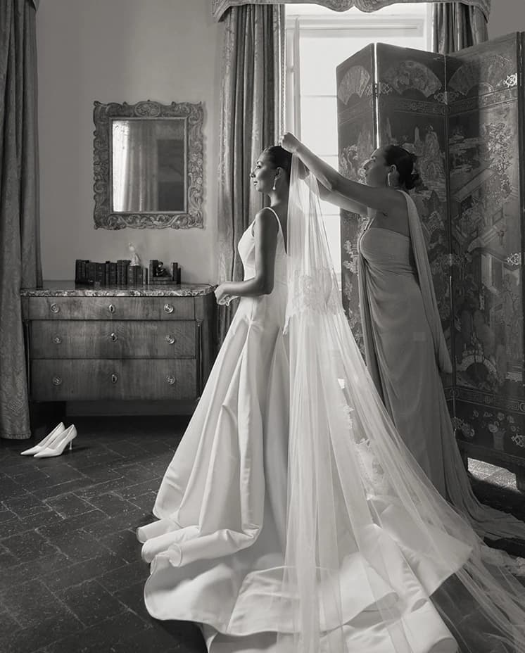 A bridal preparation moment with the bride in a minimalist gown as her veil is gently adjusted, creating a soft, elegant silhouette.