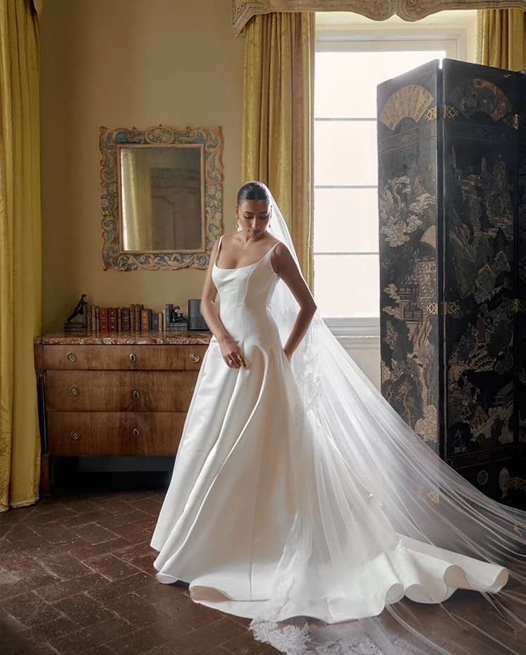 A bride in a minimalist gown with a long sheer veil, softly posed in a historic villa interior.