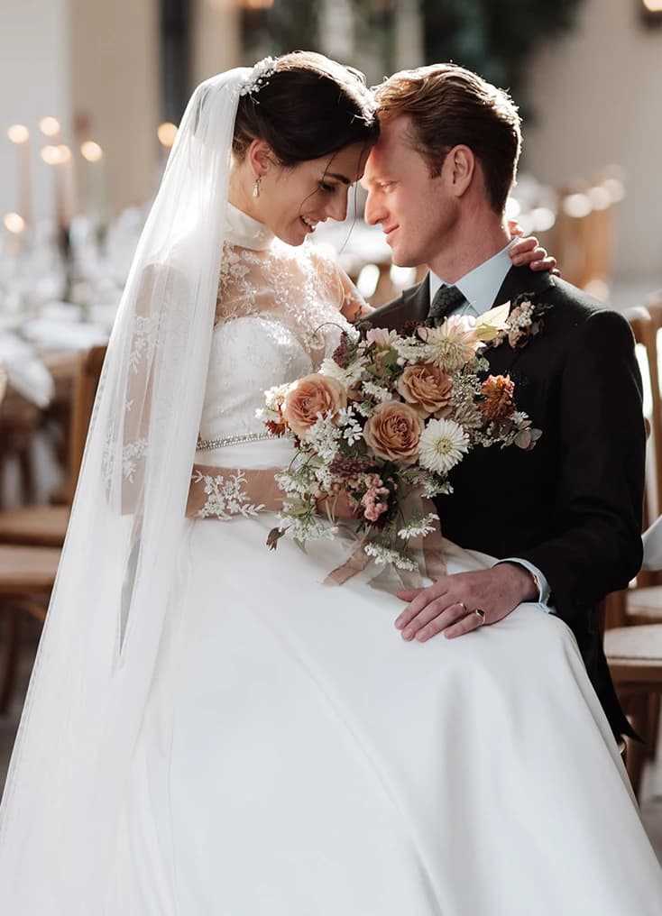 Bride and groom embracing during their wedding ceremony, holding a bouquet of flowers in a romantic, candlelit setting.  Select 75 more words to run Humanizer.