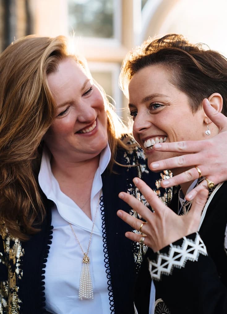 Two women smiling and admiring a wedding ring, capturing a joyful and intimate moment during a wedding celebration. 