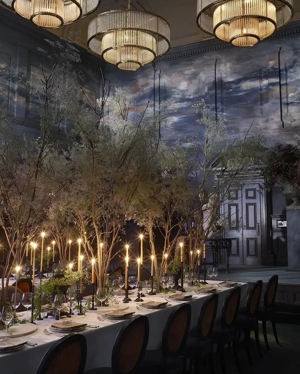 Luxury wedding reception at NoMad London with candlelit tables, indoor trees, and grand chandeliers in a dramatic setting