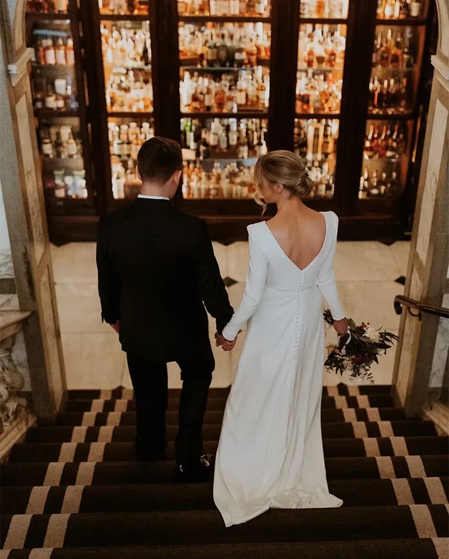 Bride and groom at Rosewood London walking down staircase with elegant bar backdrop in a luxury wedding venue