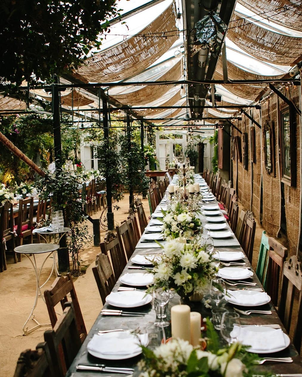 Wedding reception at Petersham Nurseries London with long banquet table, greenery, and rustic glasshouse setting