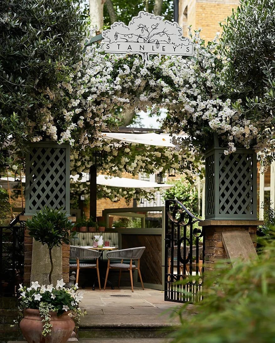Stanley’s Chelsea London wedding venue entrance with flower-covered arch, greenery, and garden dining area