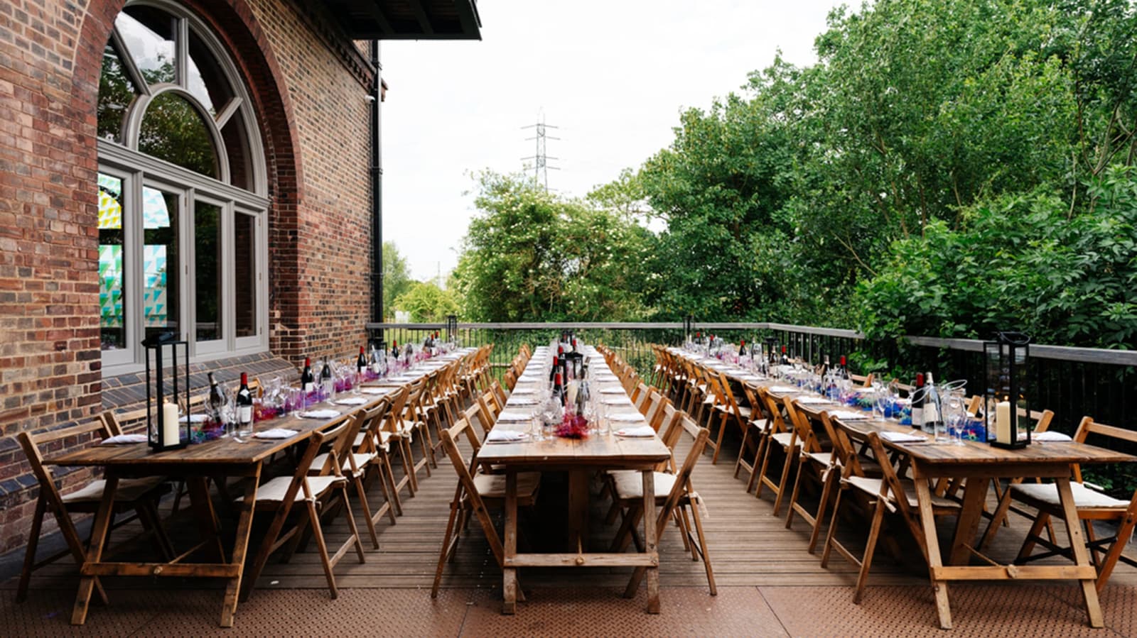 Outdoor wedding reception at The Engine House Walthamstow Wetlands London with long tables, wooden seating, and riverside views