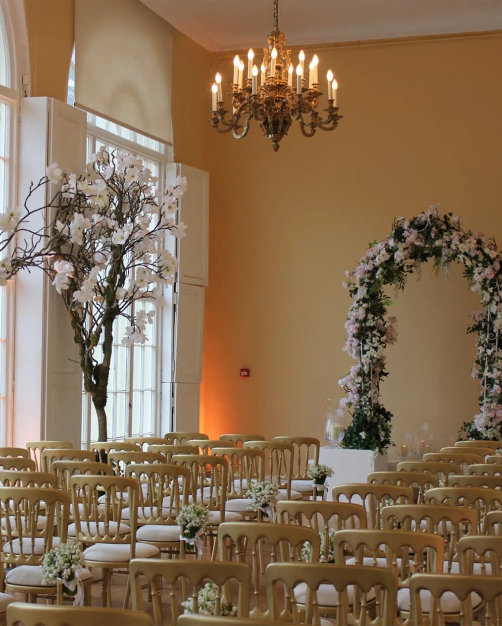 Elegant wedding ceremony at Kenwood House featuring a floral arch, chandelier lighting, and a bright historic room
