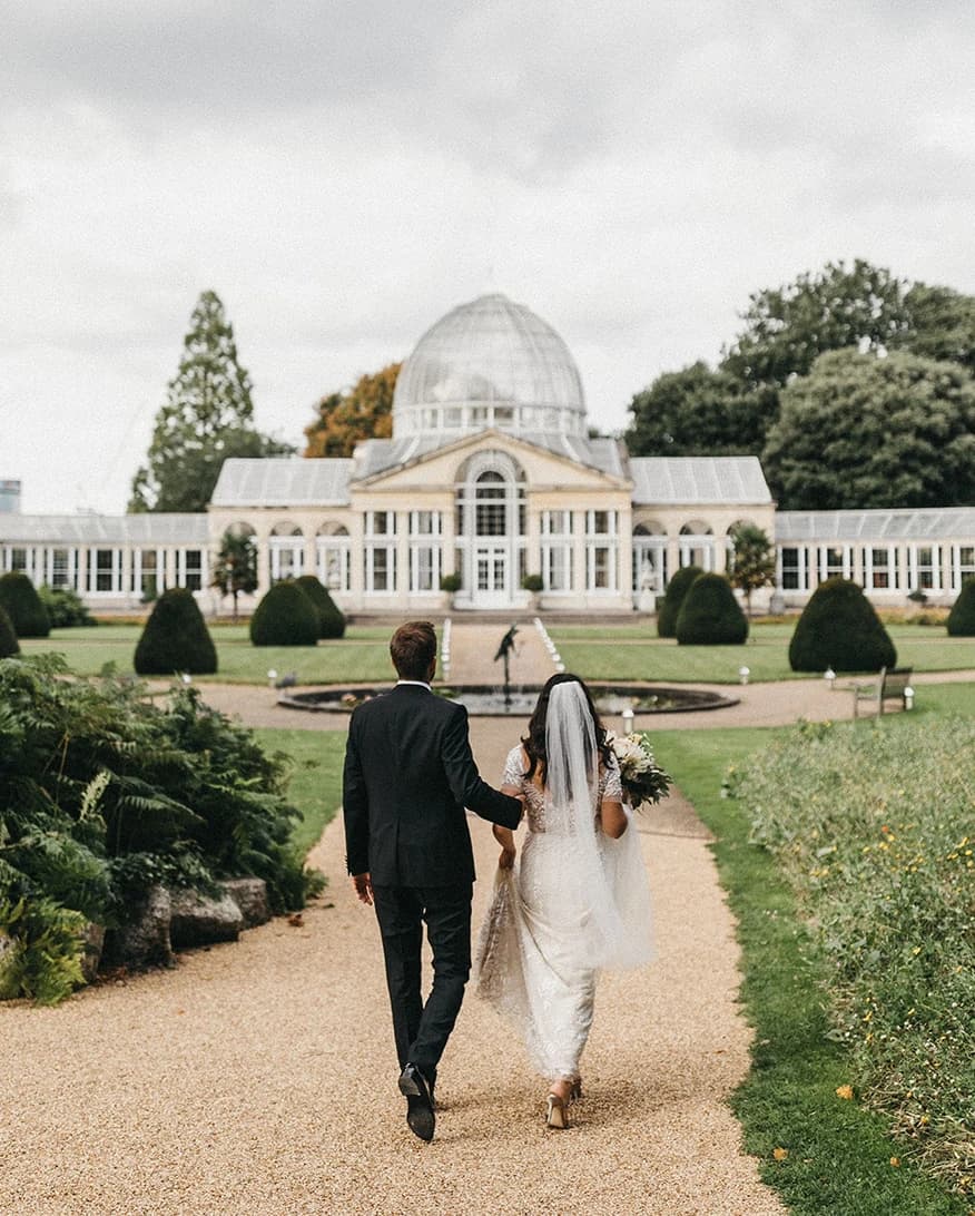 Bride and groom at Syon Park Conservatory London walking through gardens towards the grand conservatory