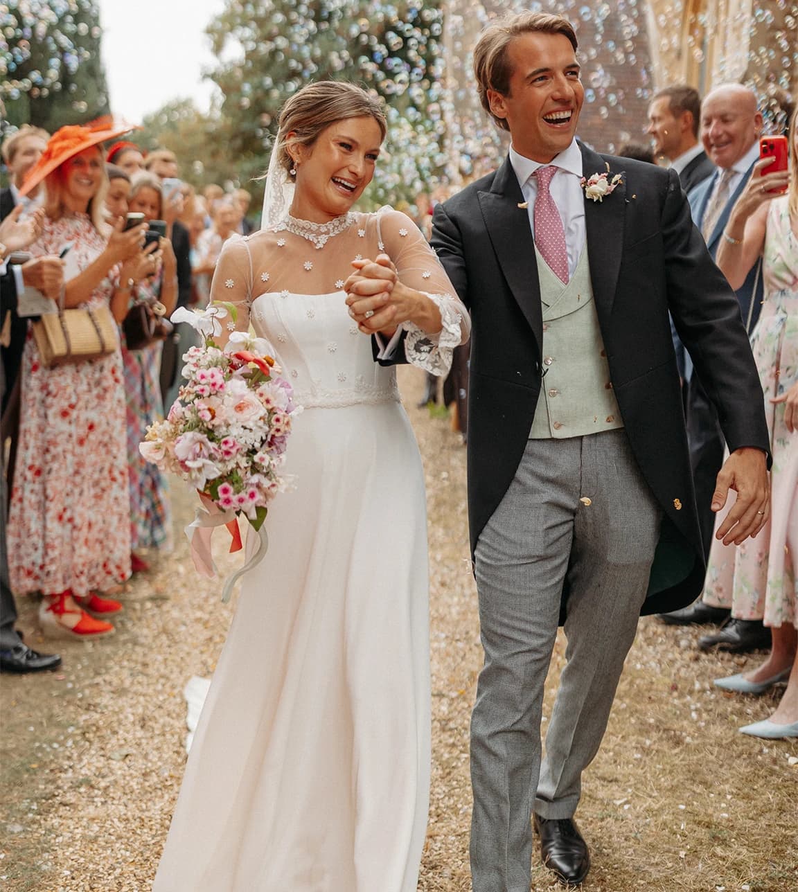 Honour & Charlie walking hand in hand after an outdoor wedding ceremony, smiling as guests celebrate and throw confetti in a countryside setting.