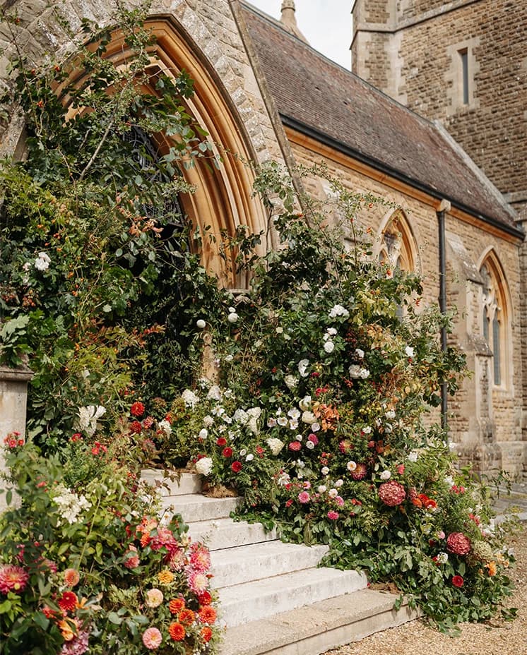 Abundant floral installation adorning the entrance of a historic countryside church for a Honour & Charlie's wedding ceremony.