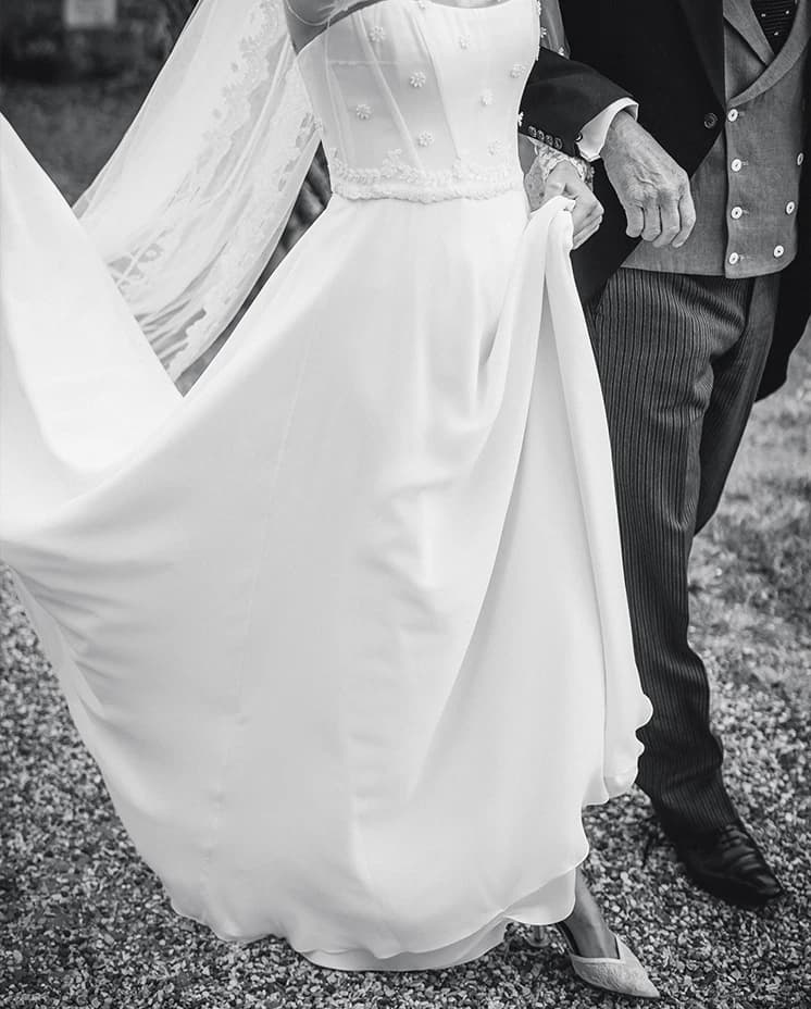 Bride walking arm in arm with her father, showcasing an elegant wedding gown and flowing veil before the ceremony.