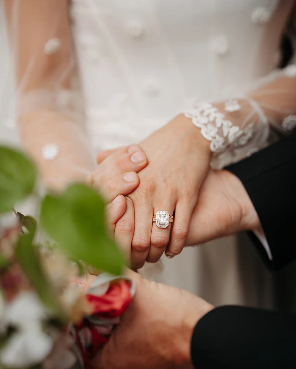 Bride and groom holding hands during their wedding ceremony, showcasing a stunning emerald-cut engagement ring from Boodles.