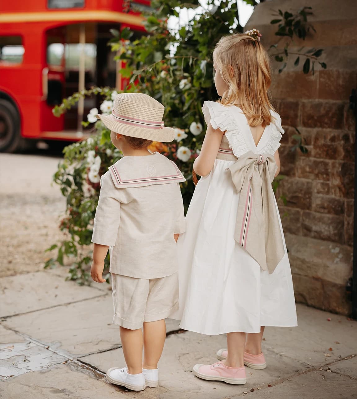Page boy wearing a classic sailor outfit and flower girl in an elegant white dress beside church flowers at a luxury English countryside wedding.