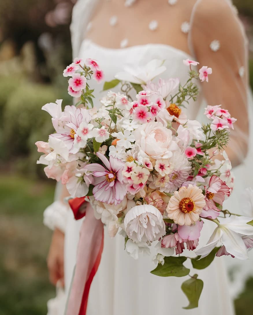 Honour holds romantic bridal bouquet featuring seasonal garden roses, cosmos, dahlias and delicate pink phlox, tied with flowing silk ribbons for a luxury countryside wedding.