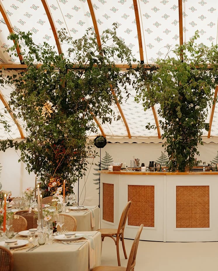 Elegant wedding bar with rattan panelling and lush greenery installations inside a luxury sailcloth marquee