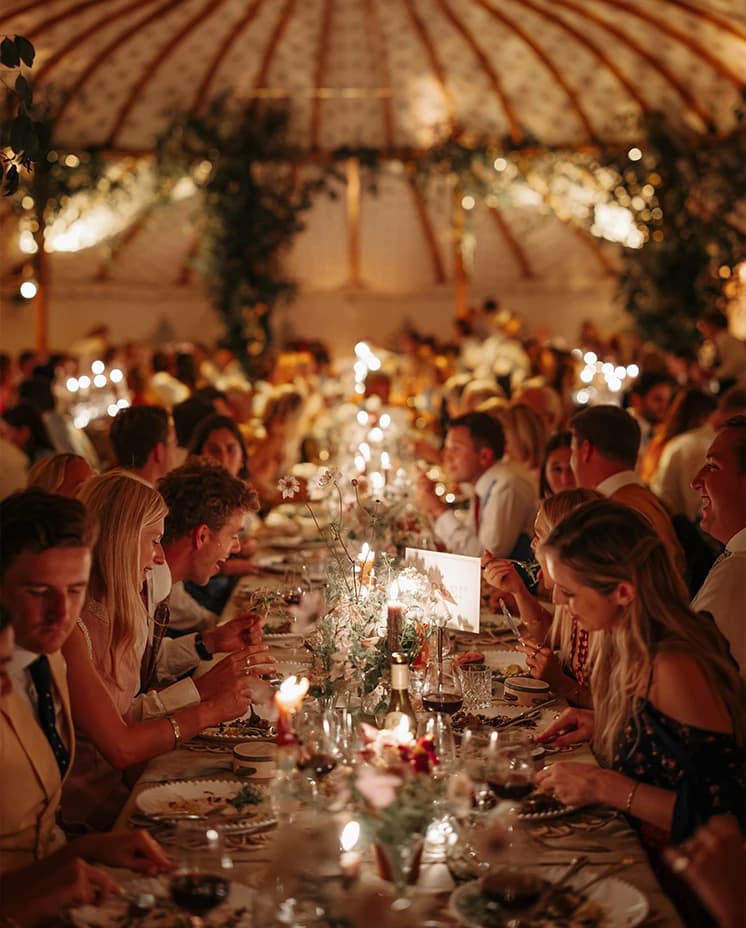 Wedding guests dining beneath suspended greenery and twinkling candlelight during an elegant marquee reception.