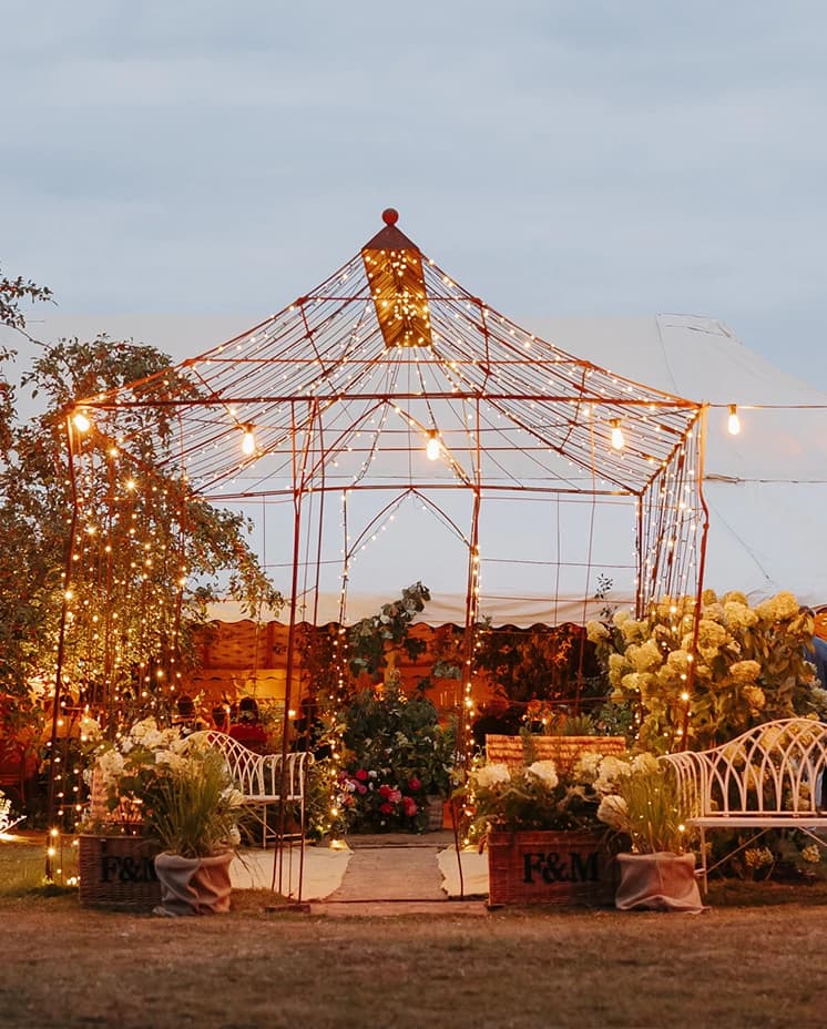 Romantic outdoor wedding lounge featuring fairy lights, floral arrangements and elegant seating for a  countryside marquee wedding.