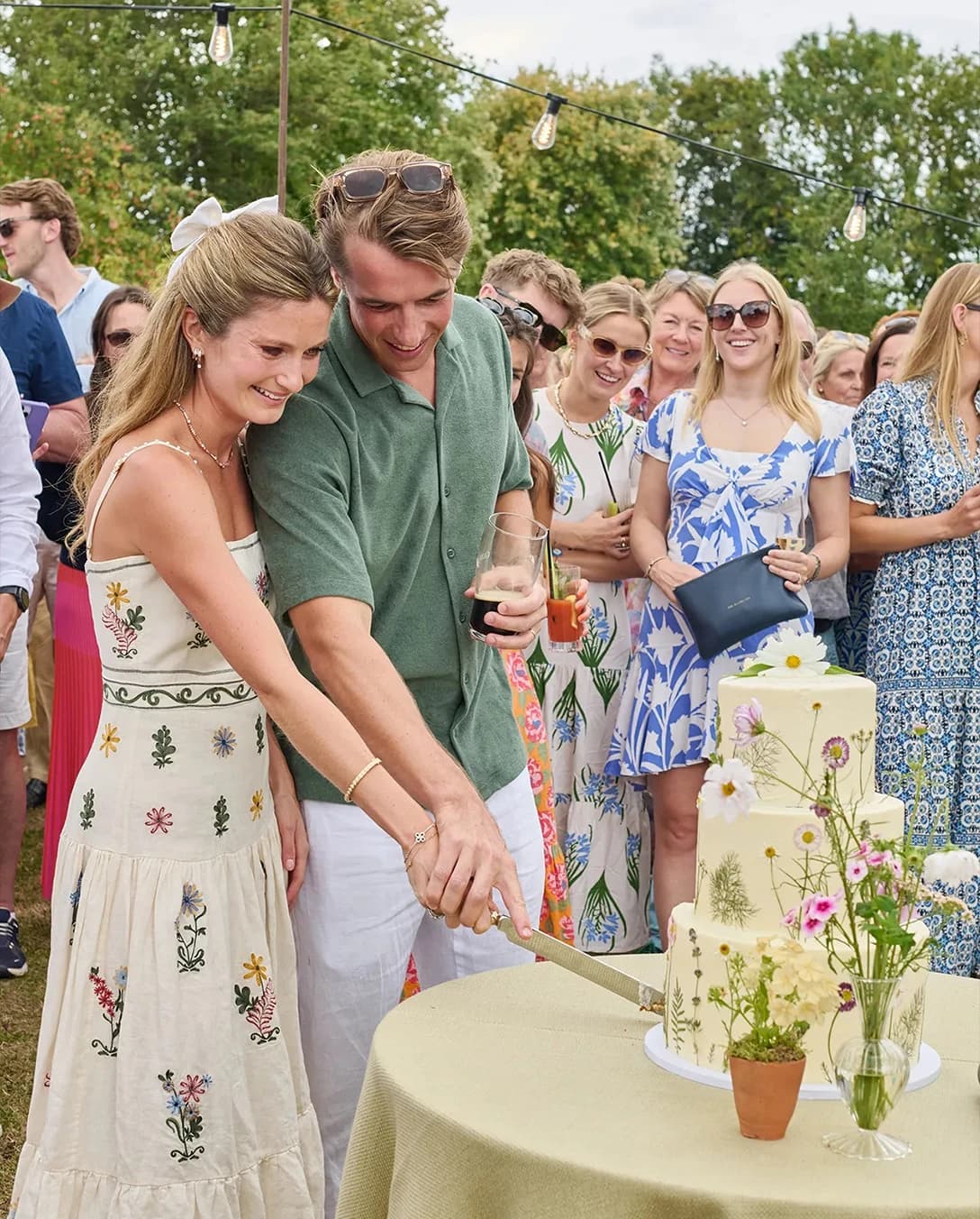Couple cutting a beautifully decorated floral wedding cake surrounded by guests on the second day of their countryside wedding celebration.