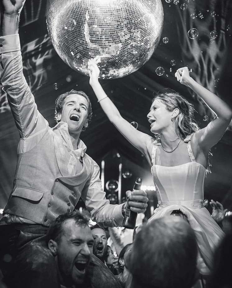 Newlyweds dancing beneath a sparkling disco ball as guests celebrate during a marquee wedding reception