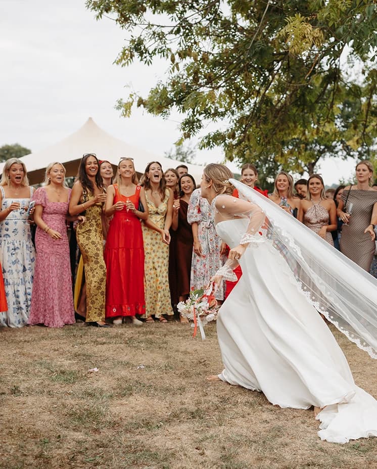 Bride preparing to toss her bouquet to a group of wedding guests during a countryside wedding reception