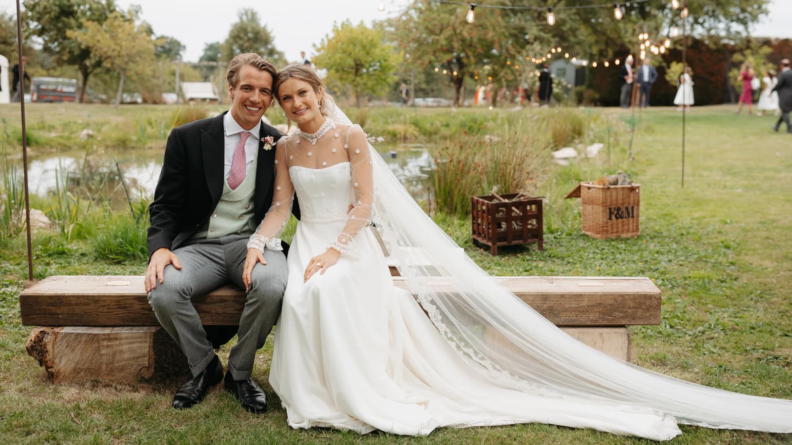 Bride and groom sitting together beside a pond during a countryside marquee wedding,