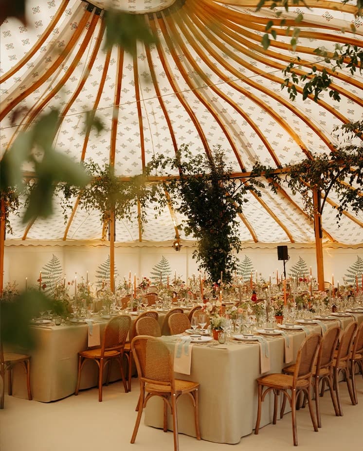 Luxury sailcloth wedding marquee featuring cascading greenery installations, elegant tablescapes, seasonal flowers and rattan chairs for a countryside wedding reception.