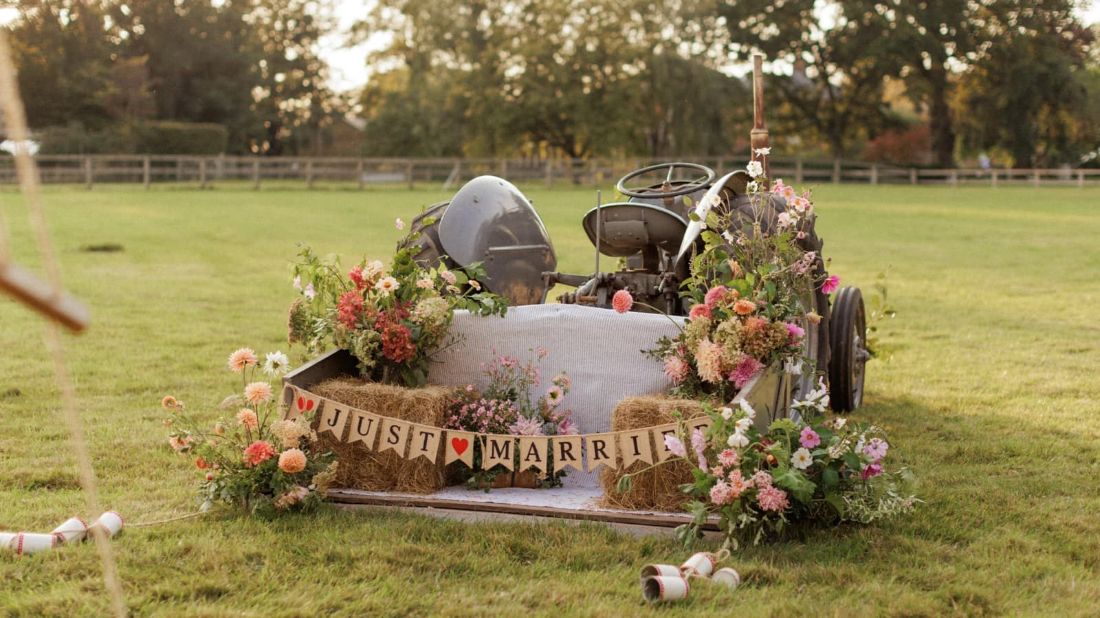 Vintage tractor decorated with colourful wedding flowers and a "Just Married" sign, creating a charming display at an English countryside wedding reception.