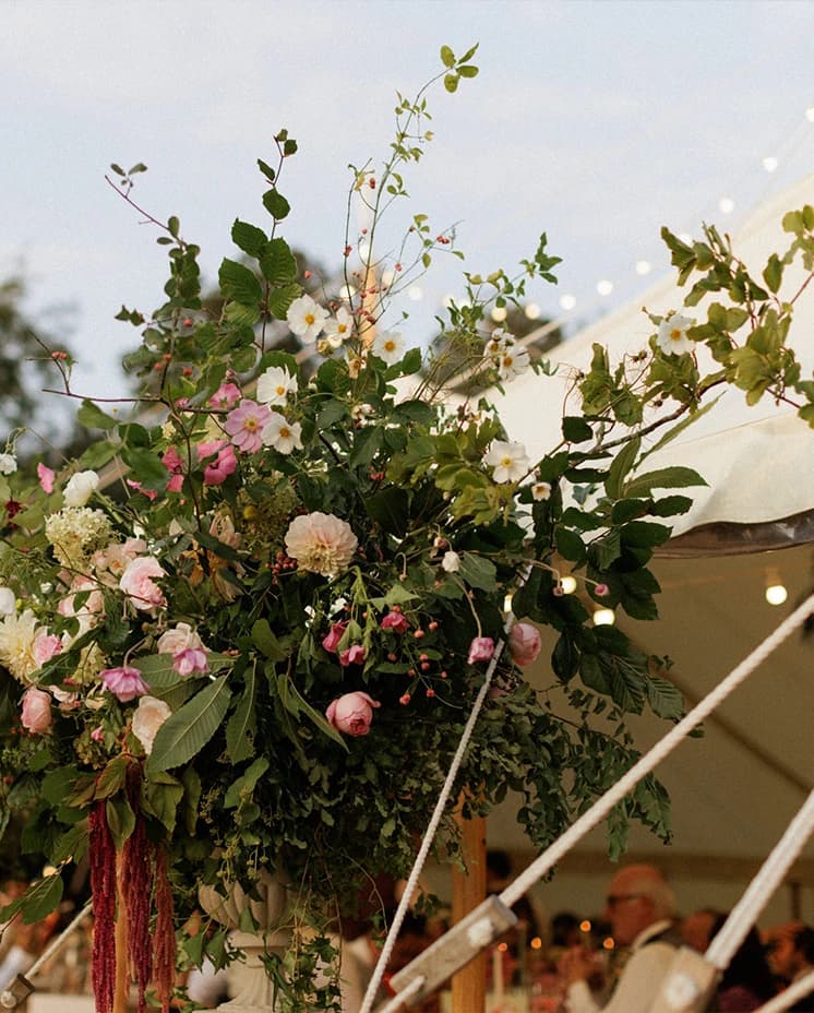 Large organic floral arrangement of pink, blush and white blooms decorating a sailcloth marquee, creating a romantic English countryside wedding reception.