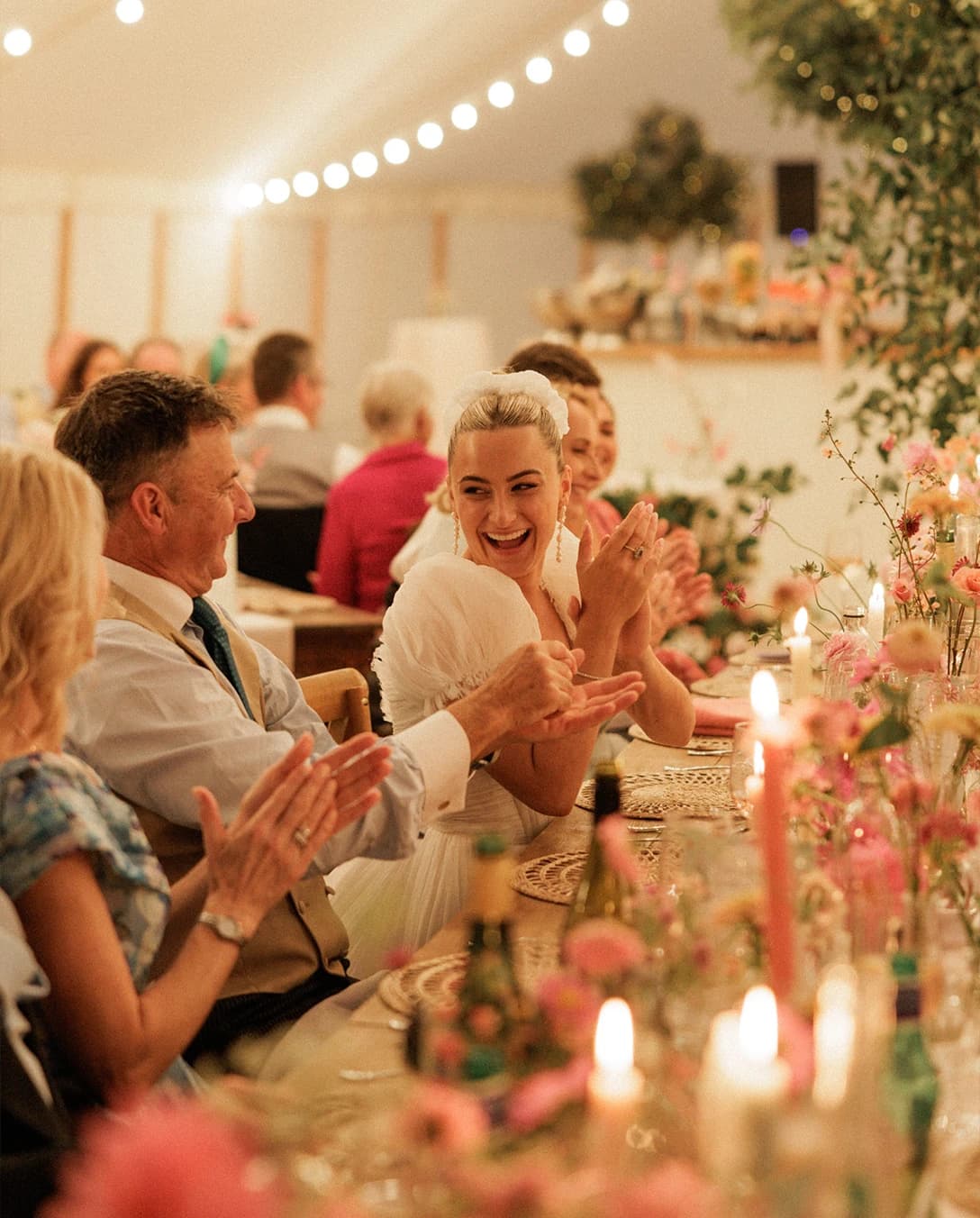 Bride laughing with family and guests during the wedding breakfast, seated at a beautifully styled reception table inside a sailcloth marquee at an English countryside wedding. 