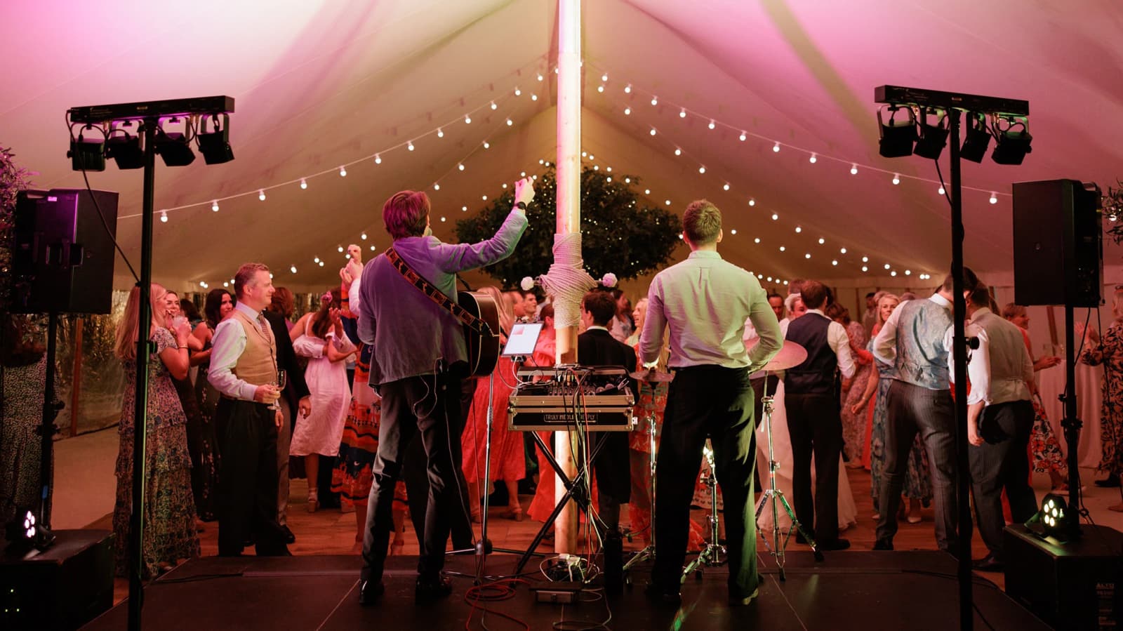 Guests dancing beneath festoon lights in a sailcloth marquee as a live wedding band performs, celebrating an unforgettable English countryside wedding reception.