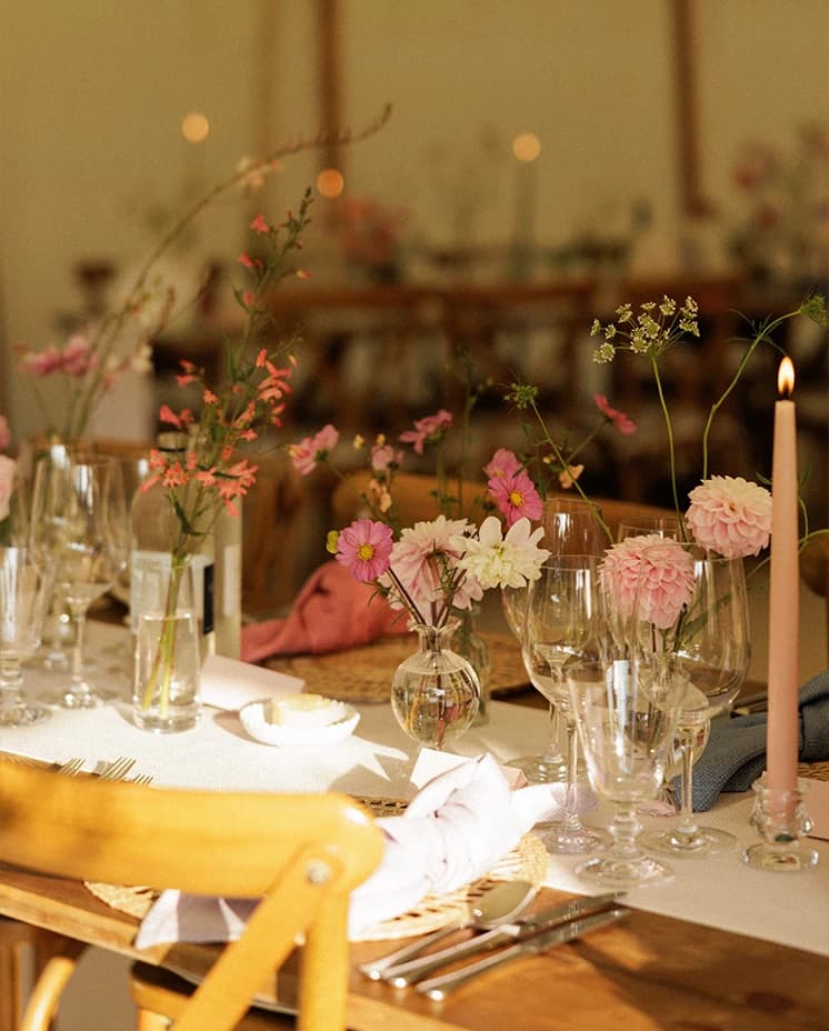 Elegant wedding reception table with delicate pink floral centrepieces, taper candles and stylish place settings inside a sailcloth marquee at an English countryside wedding.