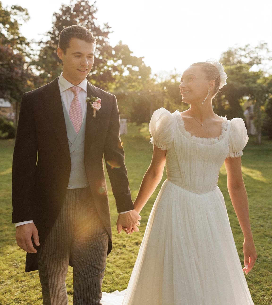 Bride and groom holding hands during golden hour at their romantic Hampshire countryside wedding, with the bride in an elegant wedding dress and the groom in a classic morning suit.