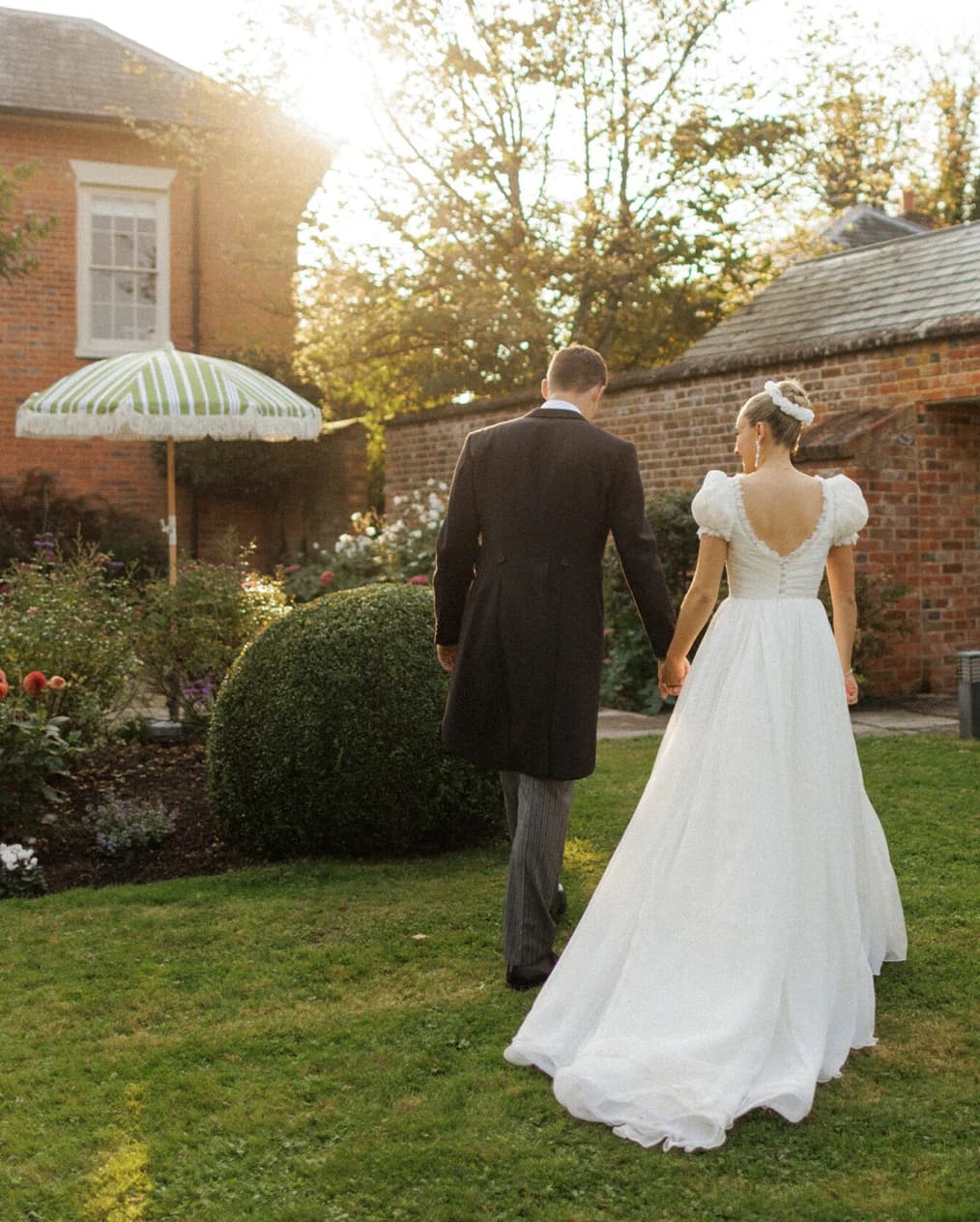 Bride and groom walking hand in hand through the gardens during golden hour at their romantic Hampshire countryside wedding, with the bride in an elegant wedding dress and the groom in a classic morning suit.