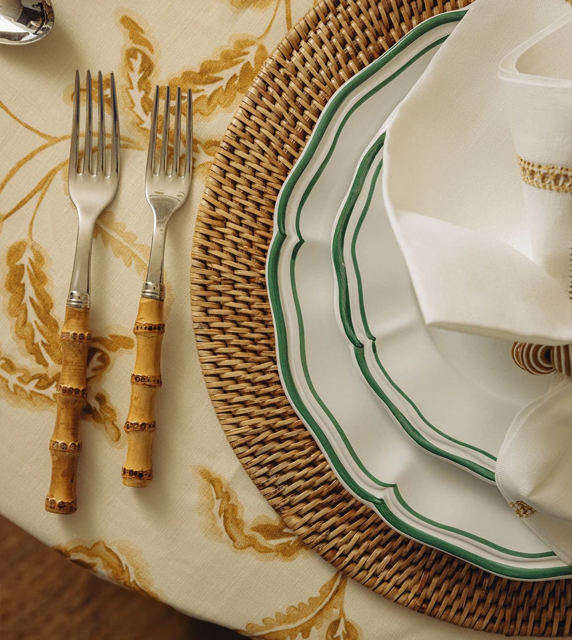 A table setting with a green-rimmed plate on a rattan placeholder